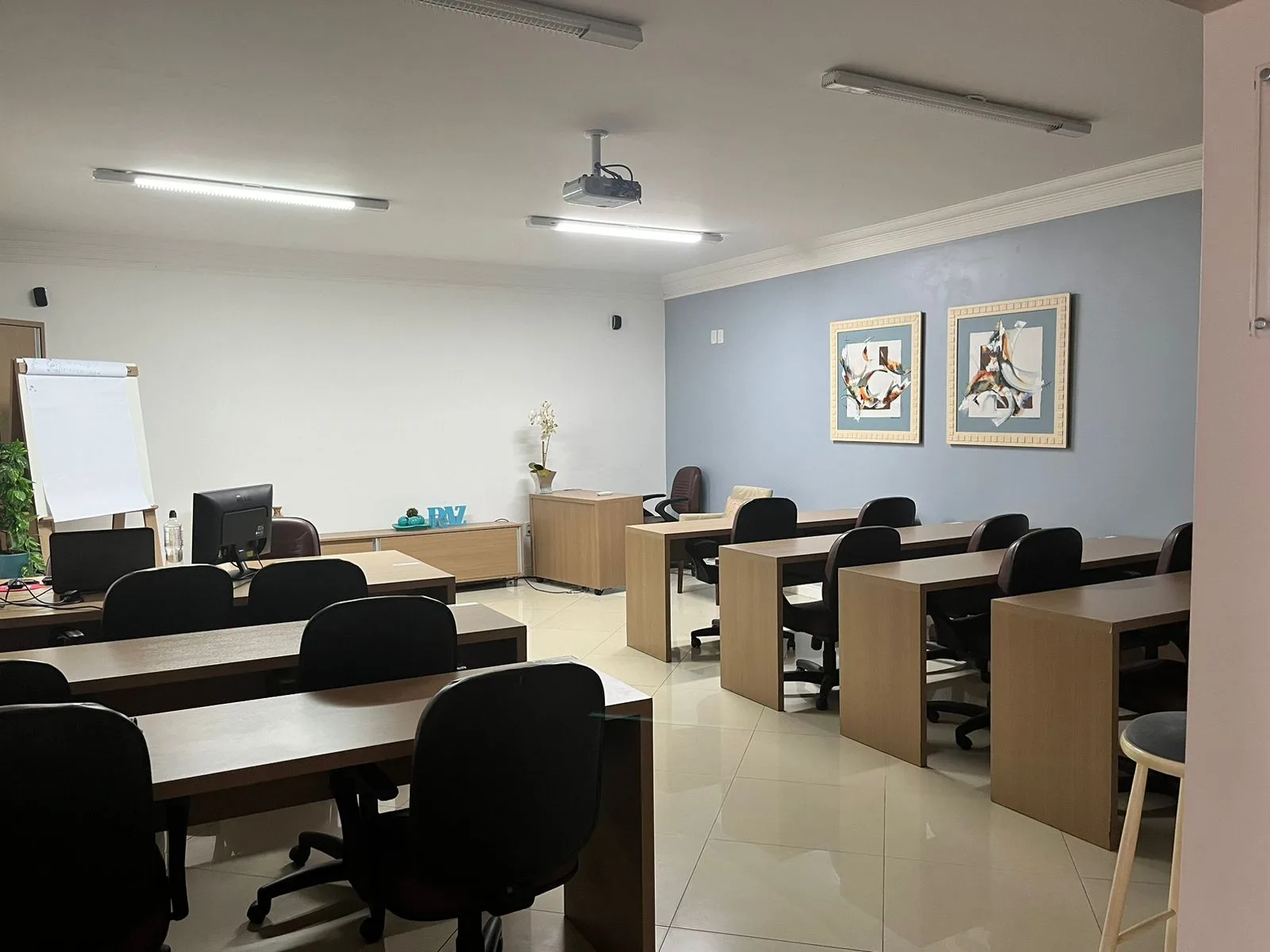 Auditório com mesas, cadeiras, projetor e flip chart